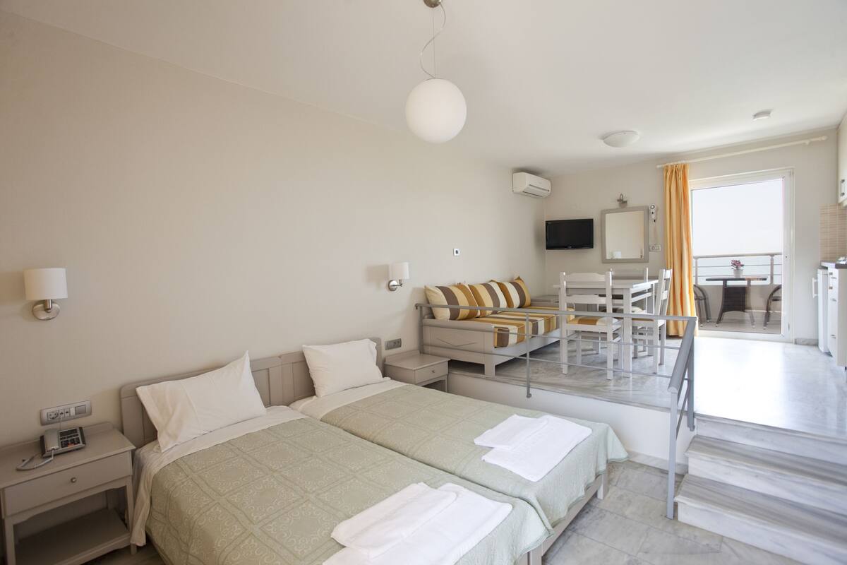 Habitación de hotel con dos camas, un escritorio, una silla, un televisor y un balcón con vistas.