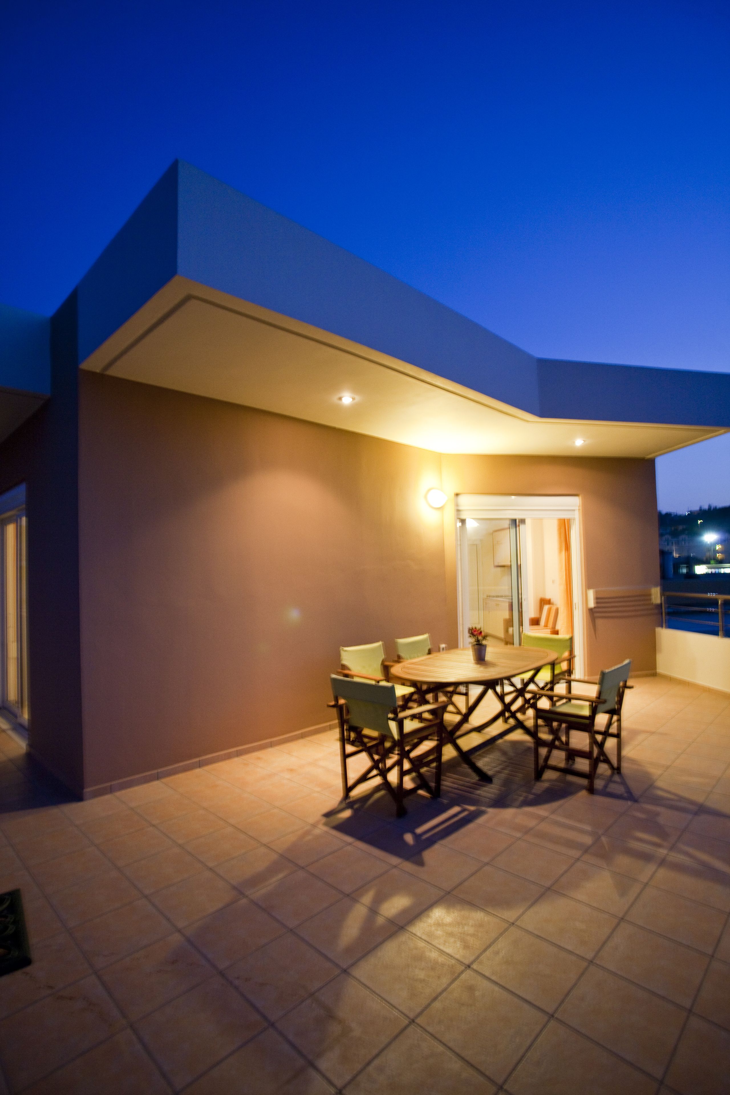 An outdoor patio with a table and chairs, a door, and a view of the city at dusk.