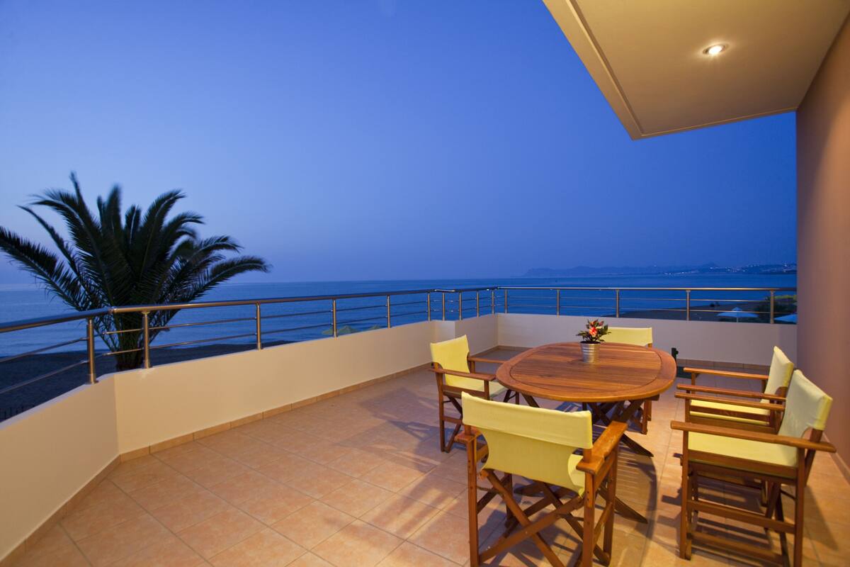 Un balcón con una mesa y sillas de madera, con vistas al mar.