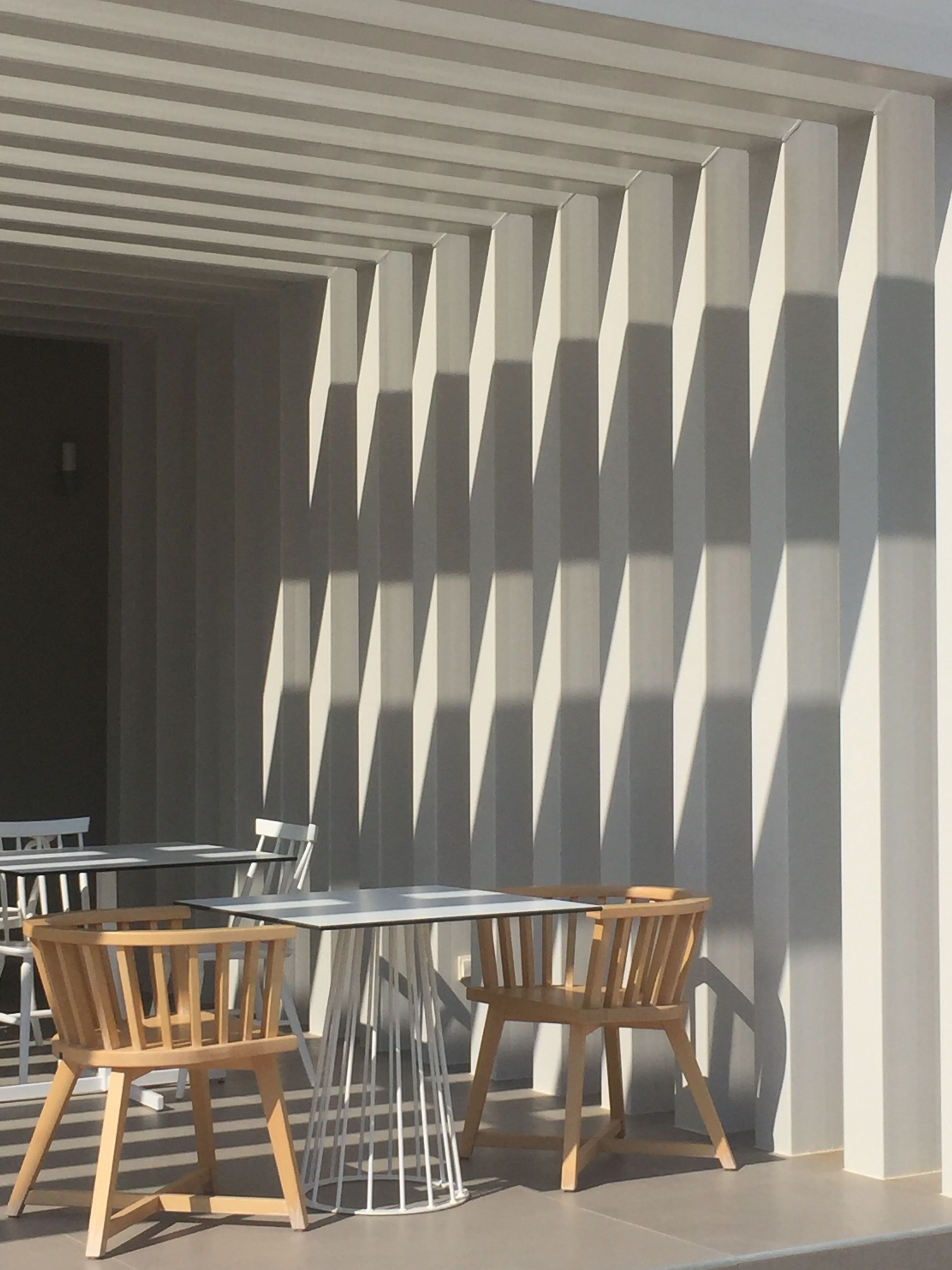 A modern outdoor seating area with tables and chairs, a patterned wall, and a clear sky.