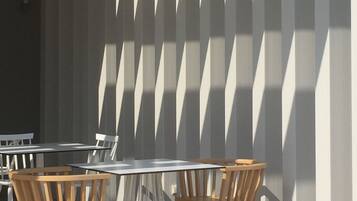 A modern outdoor seating area with tables and chairs, a patterned wall, and a clear sky.