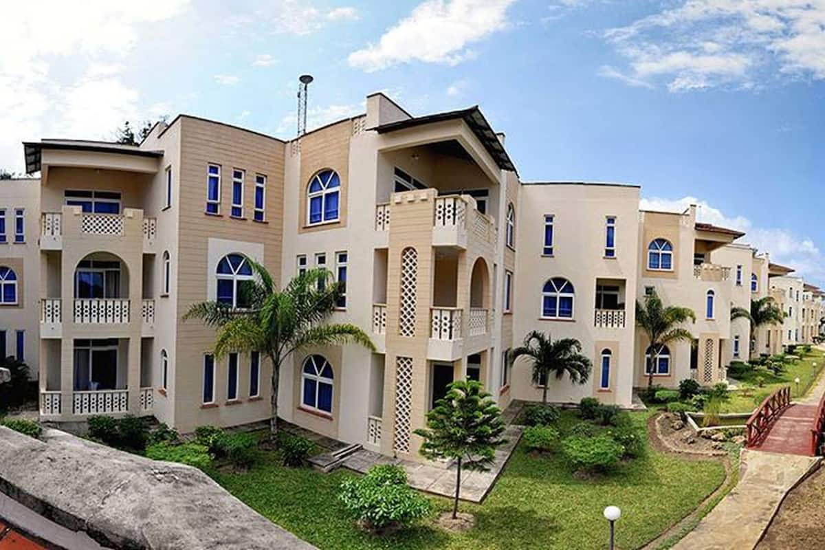 A row of modern multi-story buildings with balconies, a swimming pool, and well-maintained lawns.