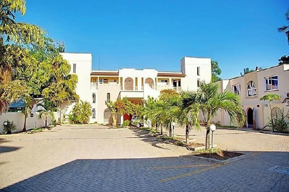 Un patio con un edificio que tiene un arco central, rodeado de palmeras y un sendero pavimentado.