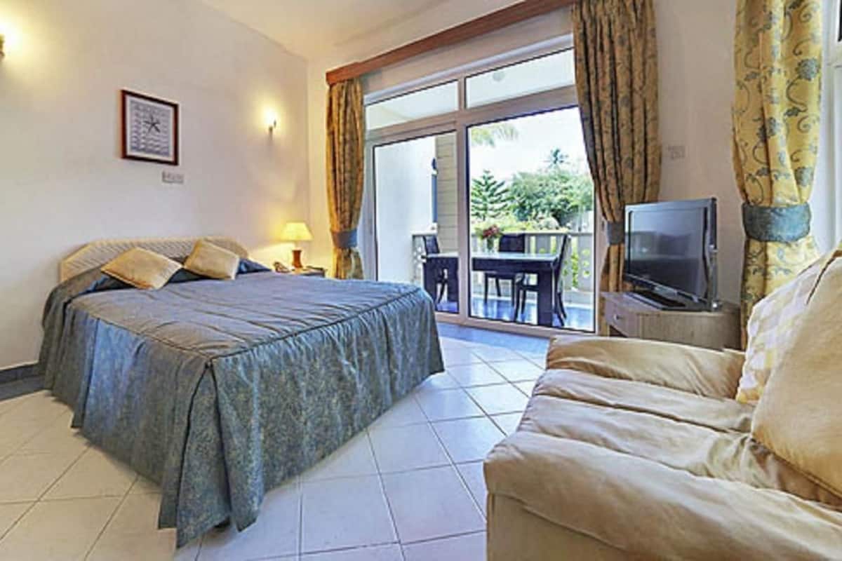 A bedroom with a bed, a TV, a sofa, a table, and a chair.