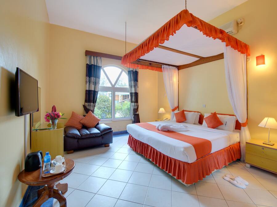 A hotel room with a four-poster bed, a sofa, a small table with a tray, and a TV mounted on the wall.