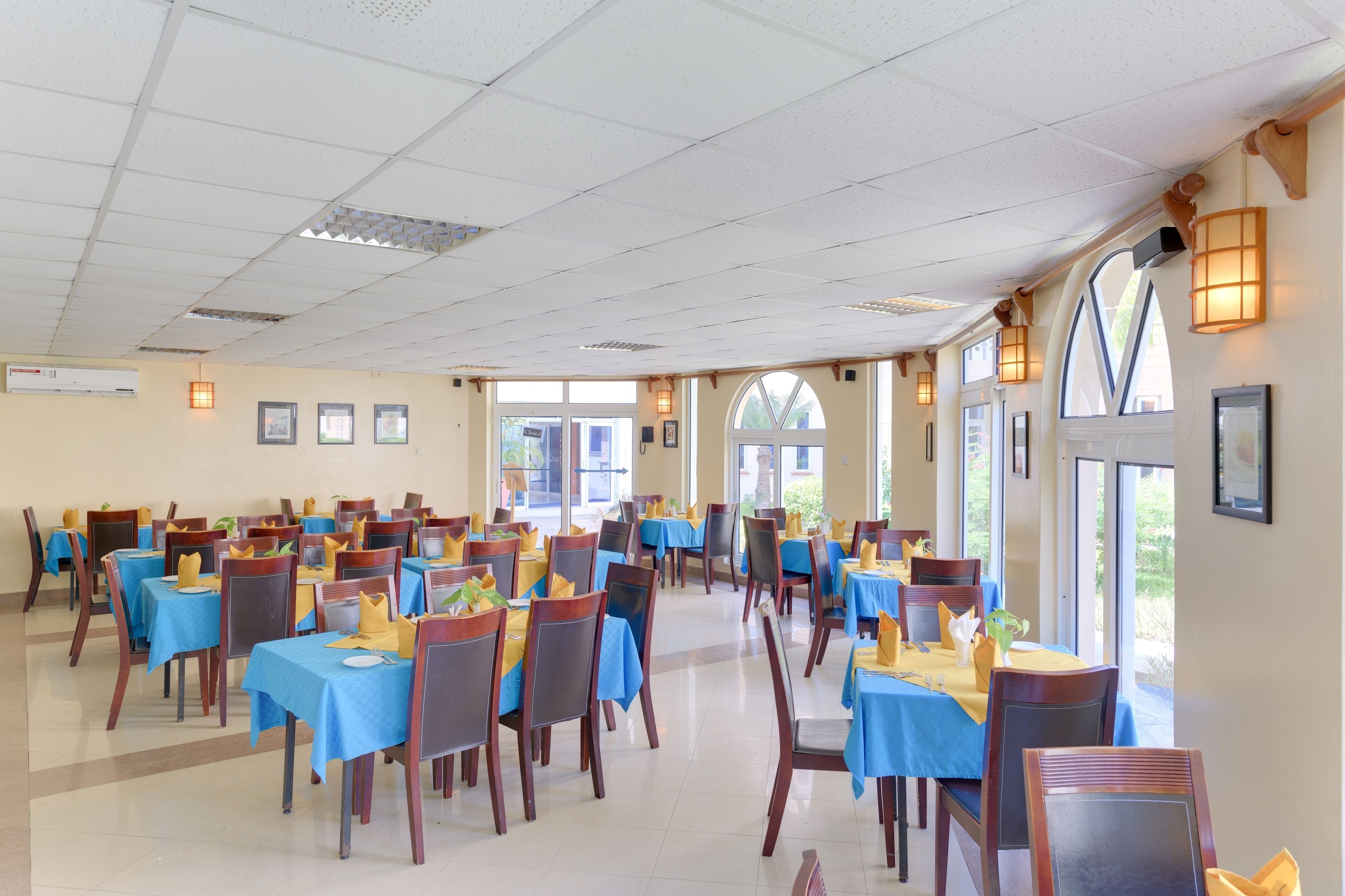 Un comedor amplio con mesas dispuestas para varios comensales, que cuenta con techos altos y ventanas grandes que dejan entrar luz natural.