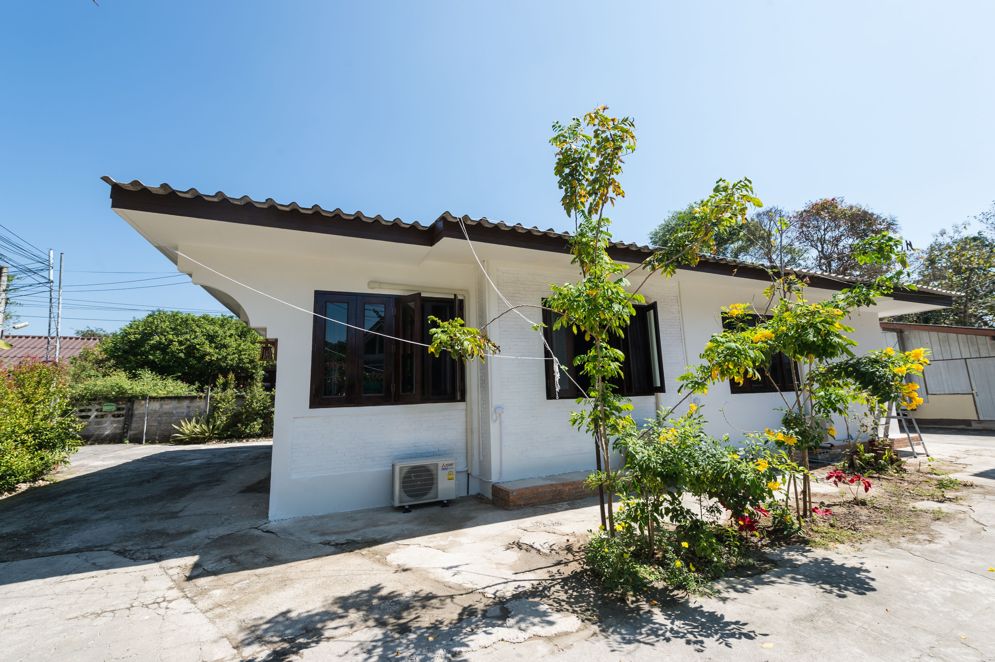 A single-story house with a tiled roof, a small porch, and a garden with various plants.