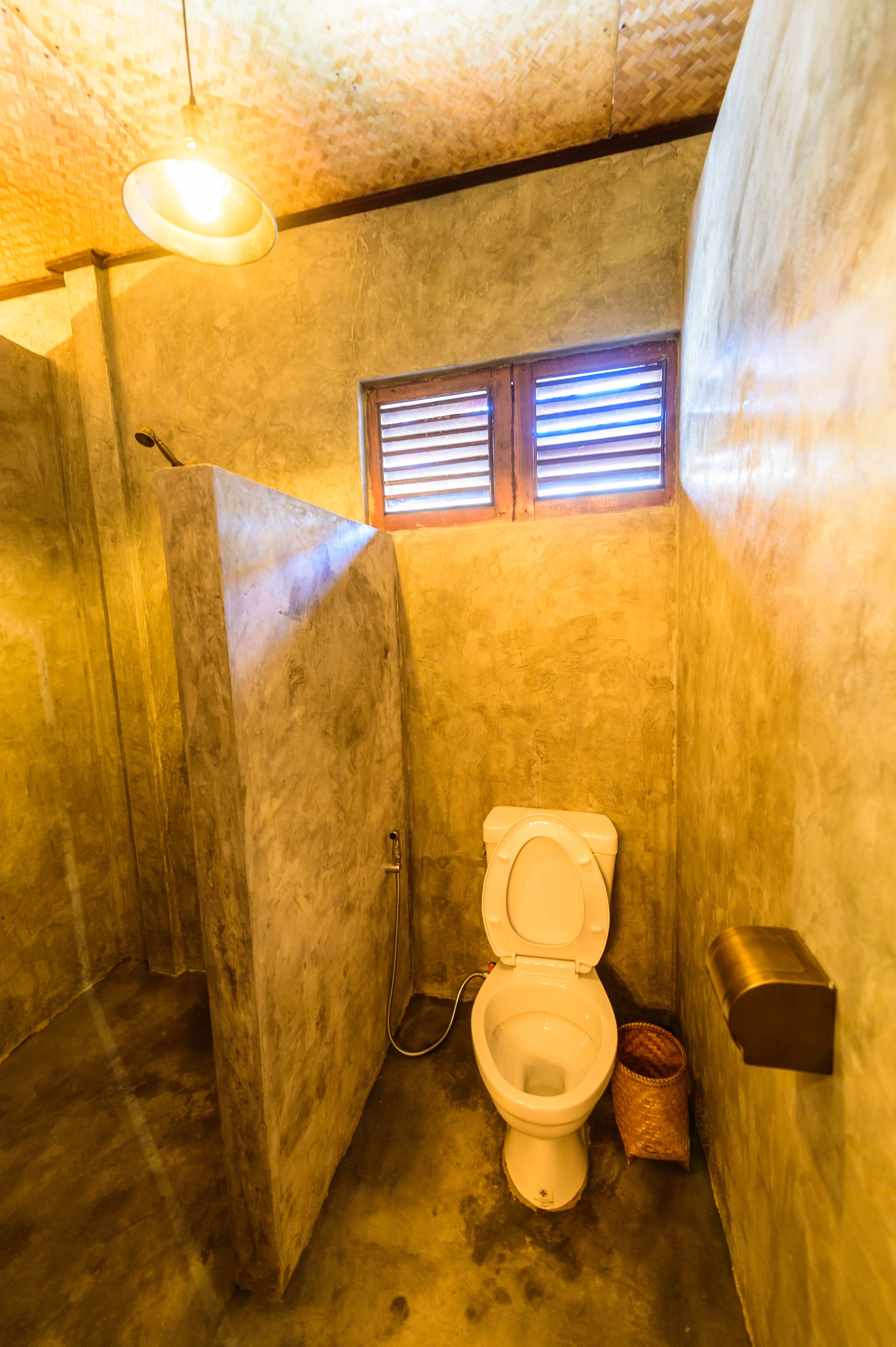 Un baño pequeño y funcional con inodoro, una ventana con persianas y un cubo de basura.