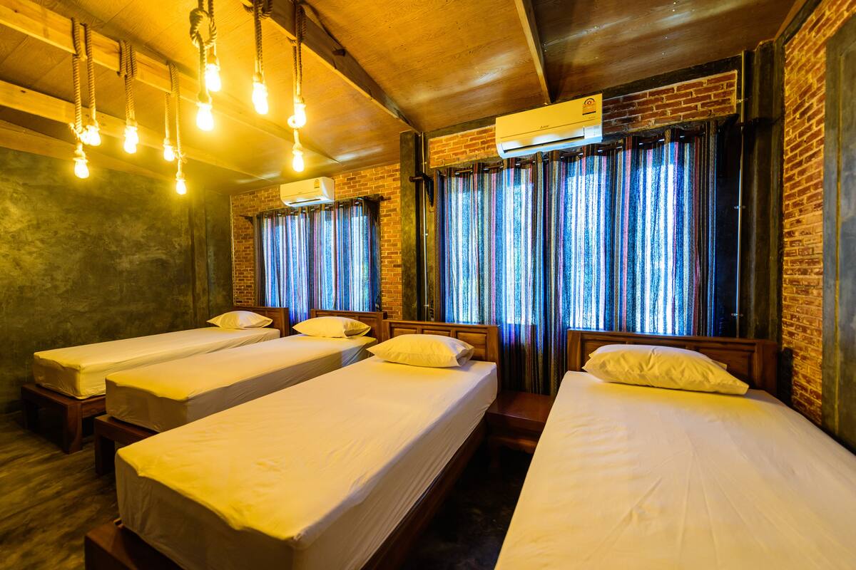 A hotel room with four single beds, wooden headboards, and a brick wall.