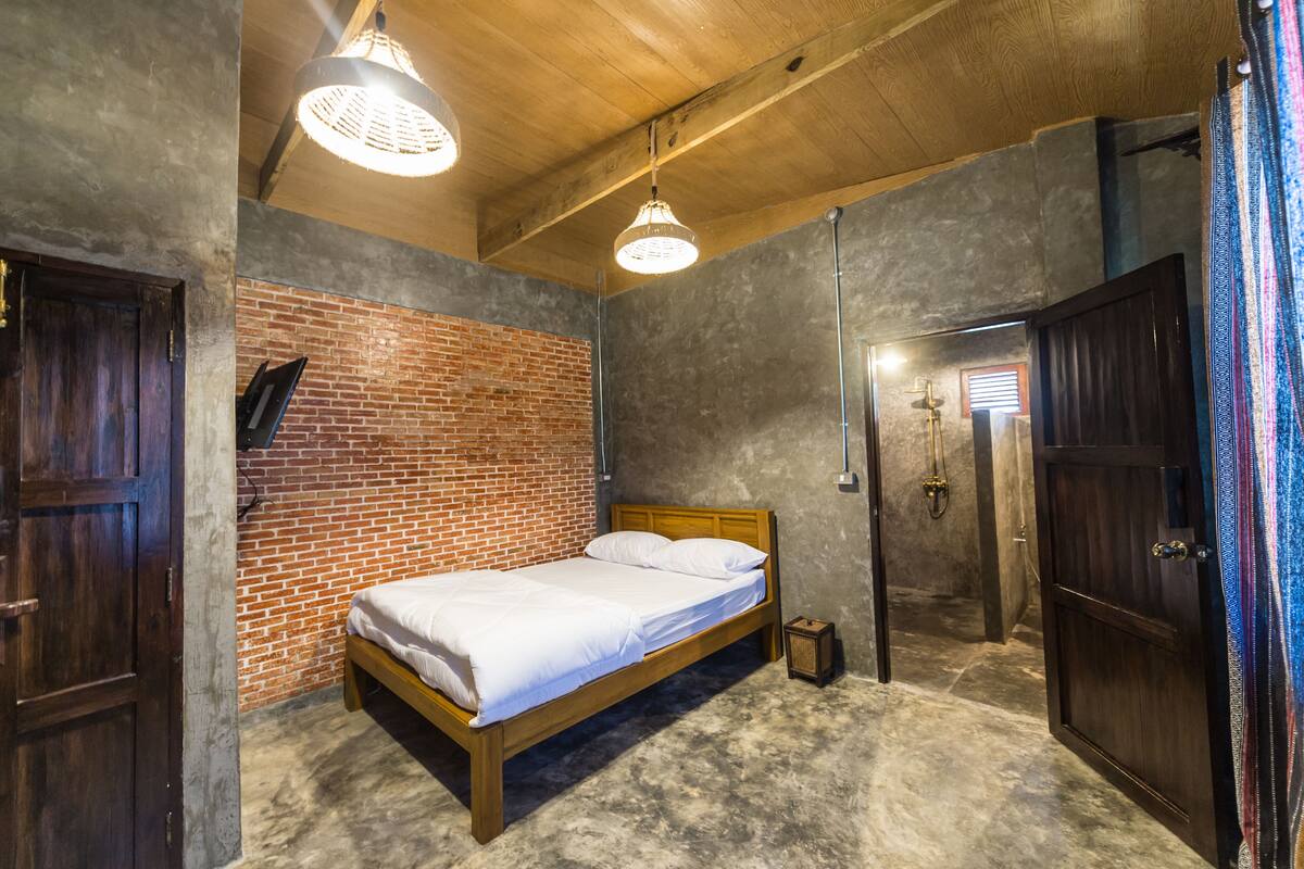 A room with a brick wall, a wooden bed, a wooden door, and a hanging light fixture.