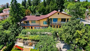 Ein zweistöckiges Haus mit rotem Dach, umgeben von üppigem Grün und einem Garten mit Rutsche und Spielbereich.