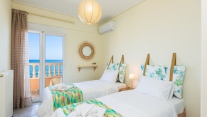 A hotel room with two beds, a balcony with a view, a hanging light fixture, and a wall-mounted air conditioner. - Birais Beach Studios (Rethymno)