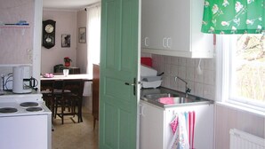 Een keuken met een fornuis, spoelbak en kasten. Er staat een eettafel met stoelen en een klok aan de muur.