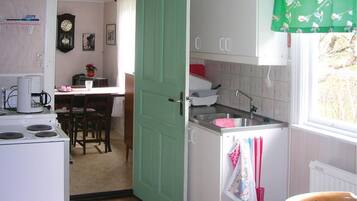 Une cuisine équipée d’une cuisinière, d’un évier et de placards. On y trouve une table à manger avec des chaises et une horloge au mur.