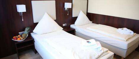 Una habitación de hotel con dos camas individuales, una mesita con fruta y lámparas de pared.