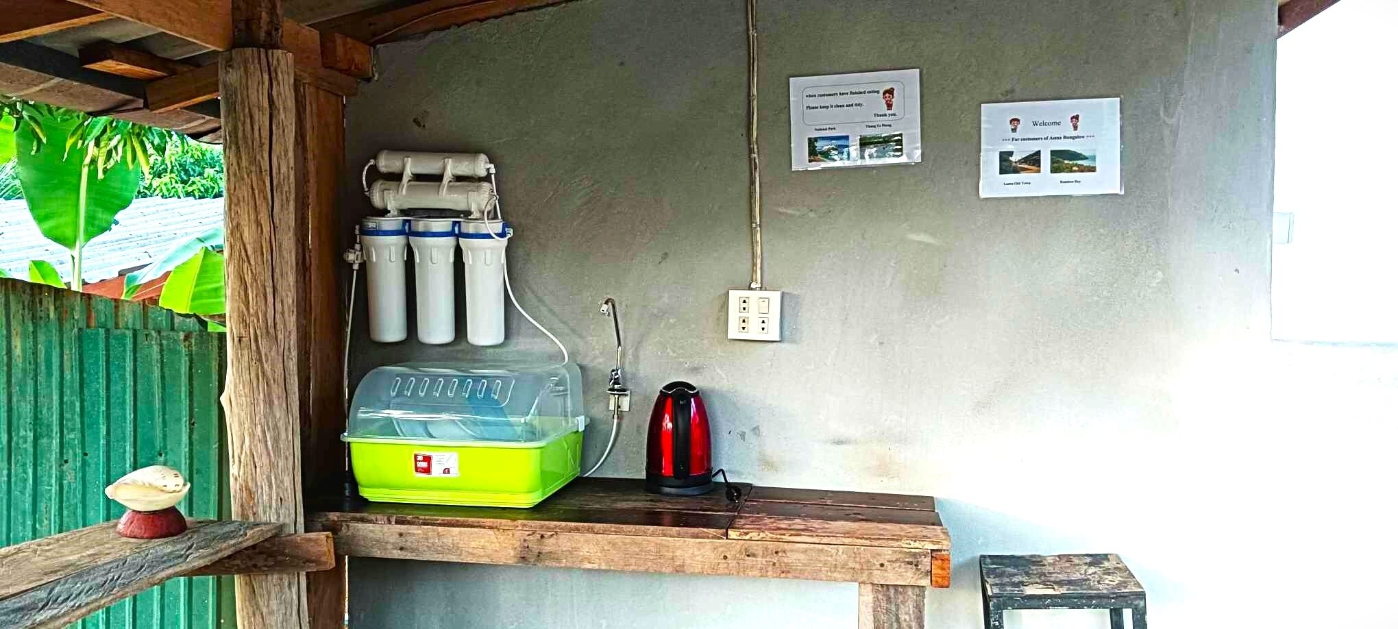 A small kitchenette with a green dish rack, a red kettle, and water filters on the wall.