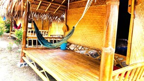Estructura de bambú con techo de paja, una hamaca y un banco de madera.