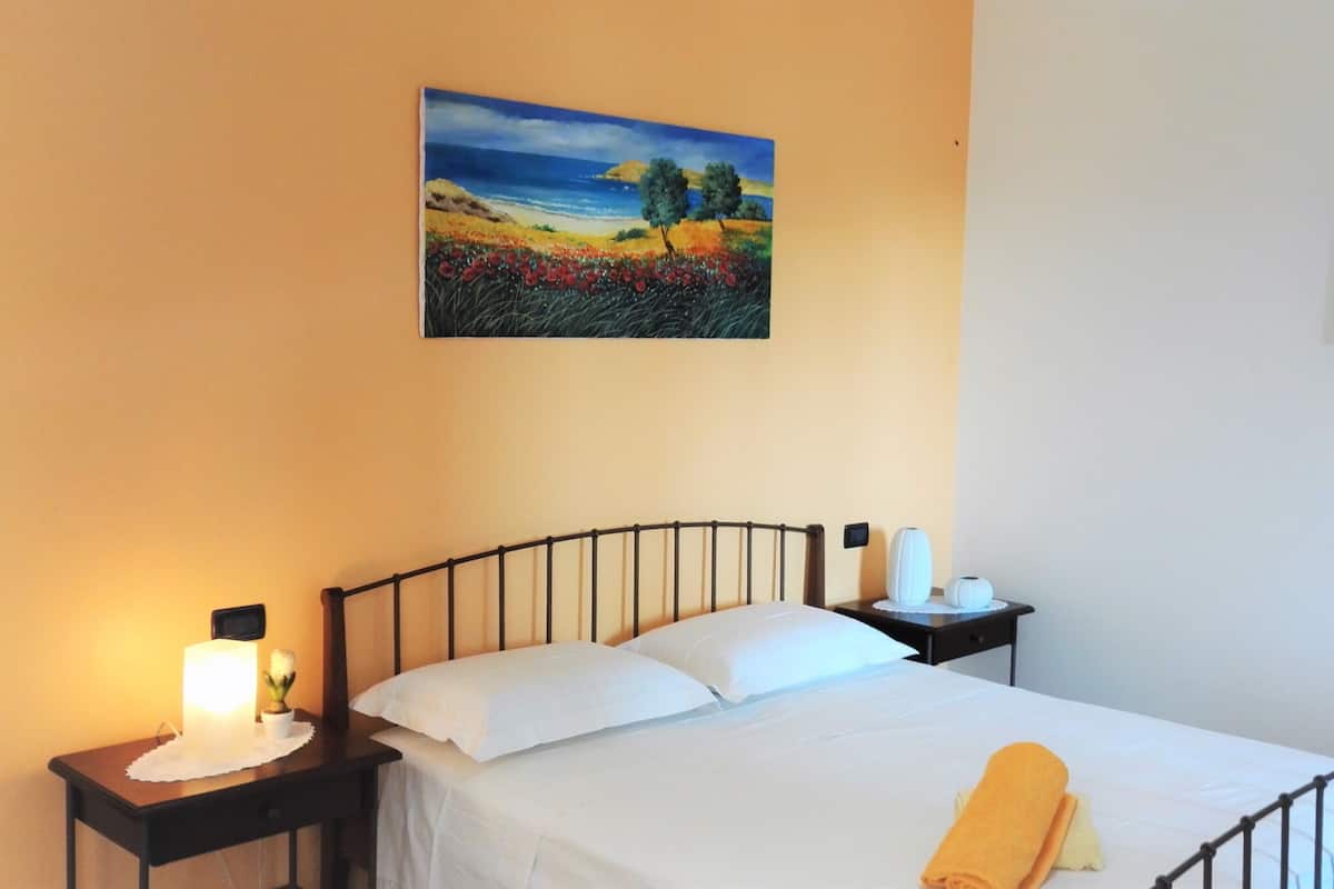 A bedroom with a bed, nightstands, a painting, and a night lamp.