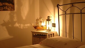 A bed with a white pillow, a small table with a ship model and a lantern, and a metal headboard. - Antico Camino (Muro Leccese)