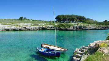 Un port aux eaux turquoise et limpides, avec deux bateaux, une côte rocheuse et, en arrière-plan, une colline boisée.