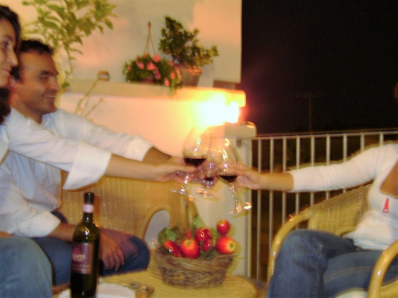 Un groupe de personnes trinquant avec des verres de vin autour d’une table sur laquelle se trouve un panier de pommes.