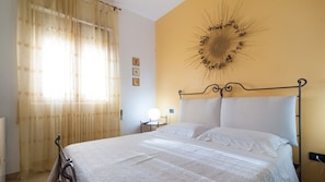 Une chambre à coucher comprenant un lit, des rideaux, un élément de décoration murale, une table de chevet avec une lampe et une prise électrique murale.