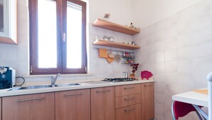 A kitchen with wooden cabinets, a stainless steel sink, and a window. - Antico Camino (Muro Leccese)