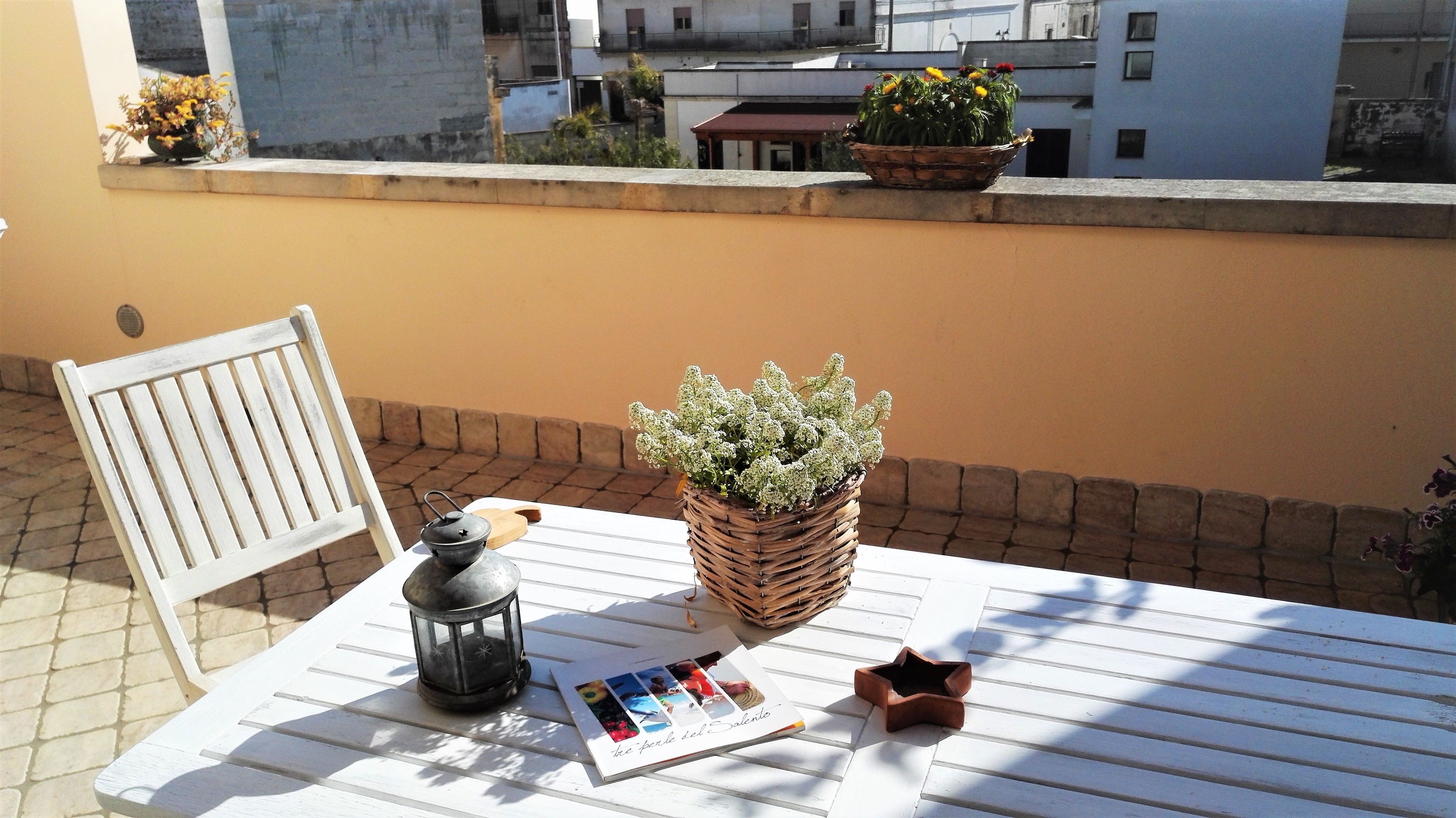 Une table avec un livre, une lanterne et une plante sur un balcon donnant sur des immeubles.