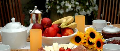 A breakfast setting with a variety of food items, including fruits, cheese, and meats, arranged on a table with a floral backdrop.