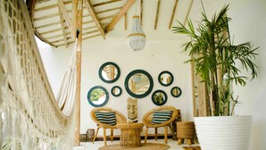Una habitación con techo alto, vigas de madera a la vista, una gran maceta blanca y varias sillas de mimbre con cojines a rayas.