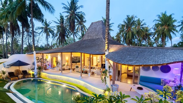Una casa moderna con piscina, mobiliario exterior y exuberante entorno tropical.