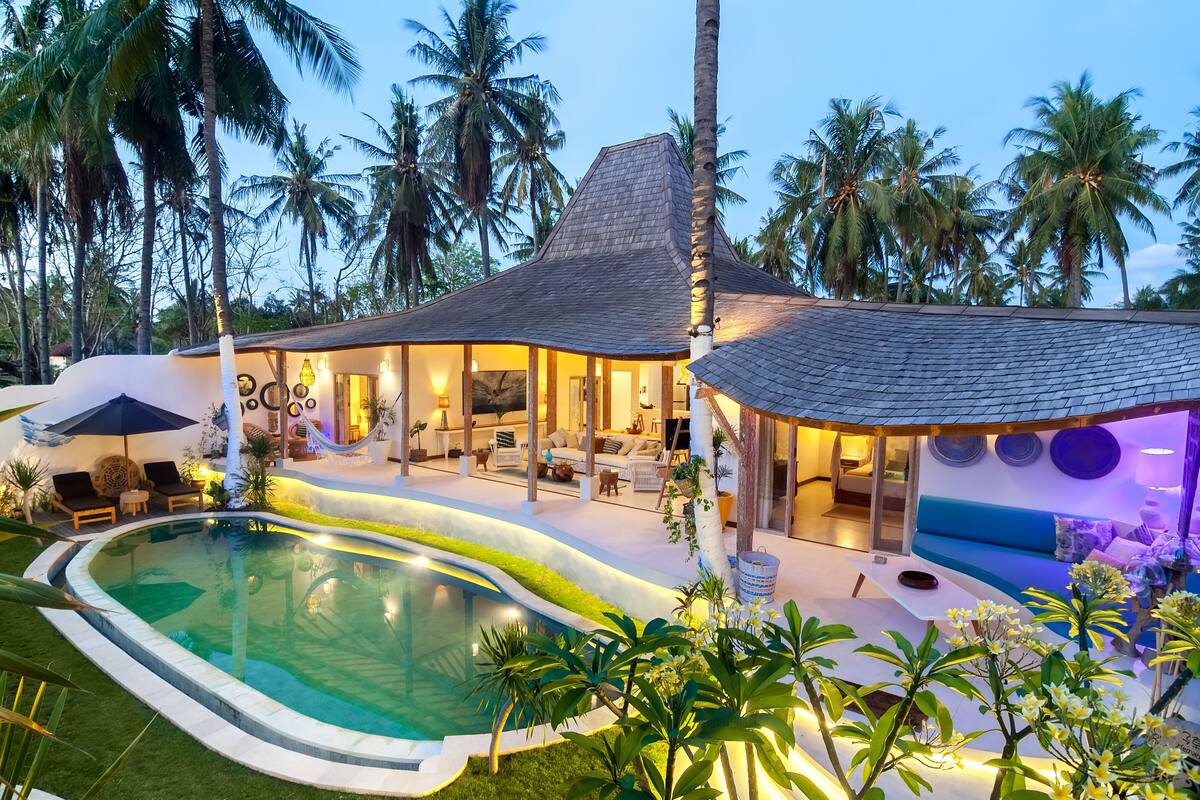 A modern house with a swimming pool, outdoor seating, and lush tropical surroundings.