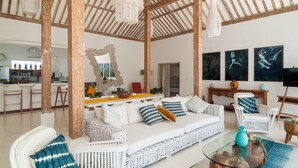 Un espacio habitable amplio con un sofá de mimbre blanco, una mesa de centro de cristal y una estructura de techo de madera.