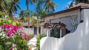 Una villa con un letrero que dice "De'Coço Villa & Suites", rodeada de exuberante follaje y palmeras.