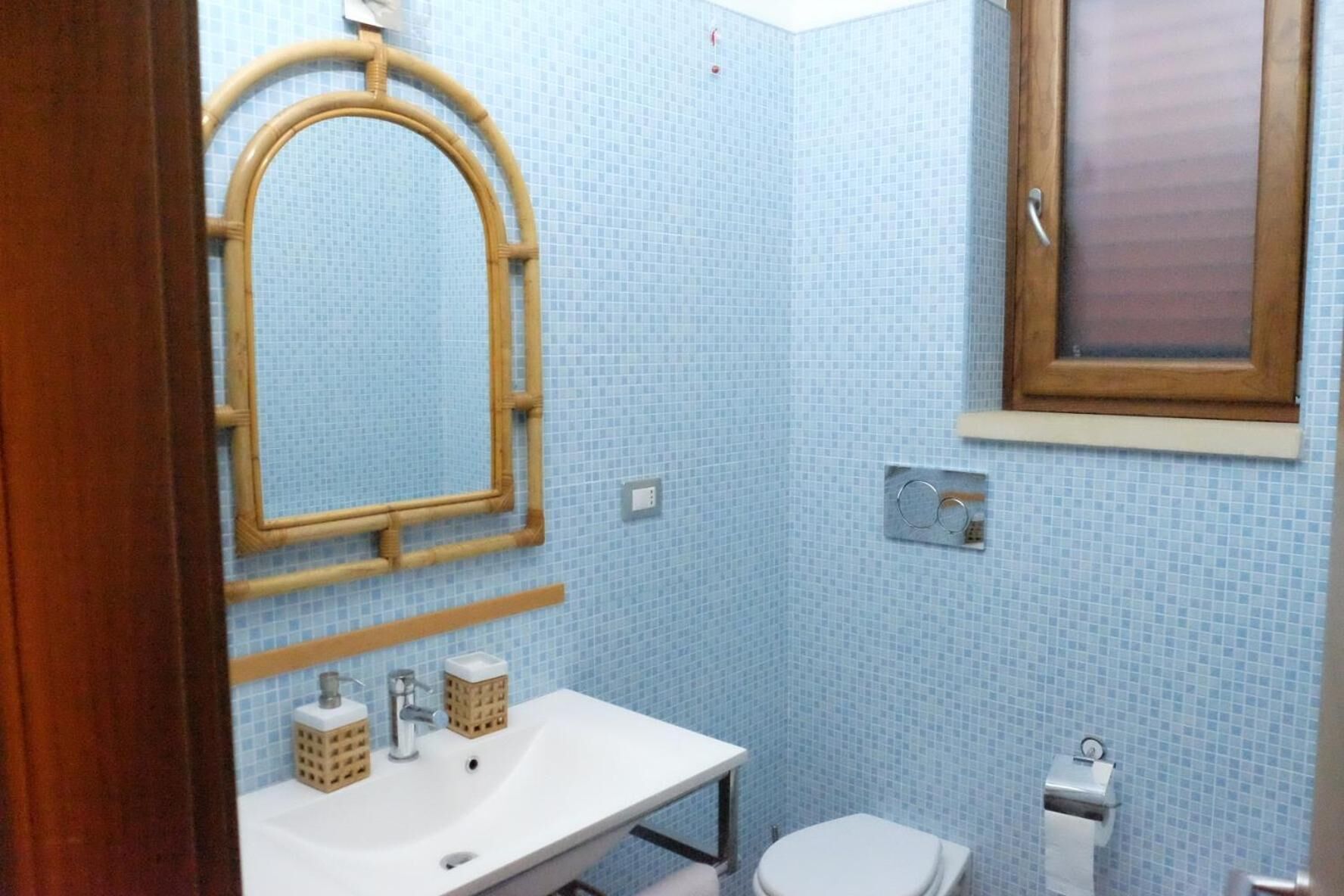 A bathroom with a white sink, a mirror, a toilet, and a window.