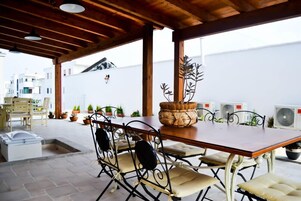 Un área de comedor al aire libre con techo de madera, sillas de metal, una mesa y plantas en macetas.