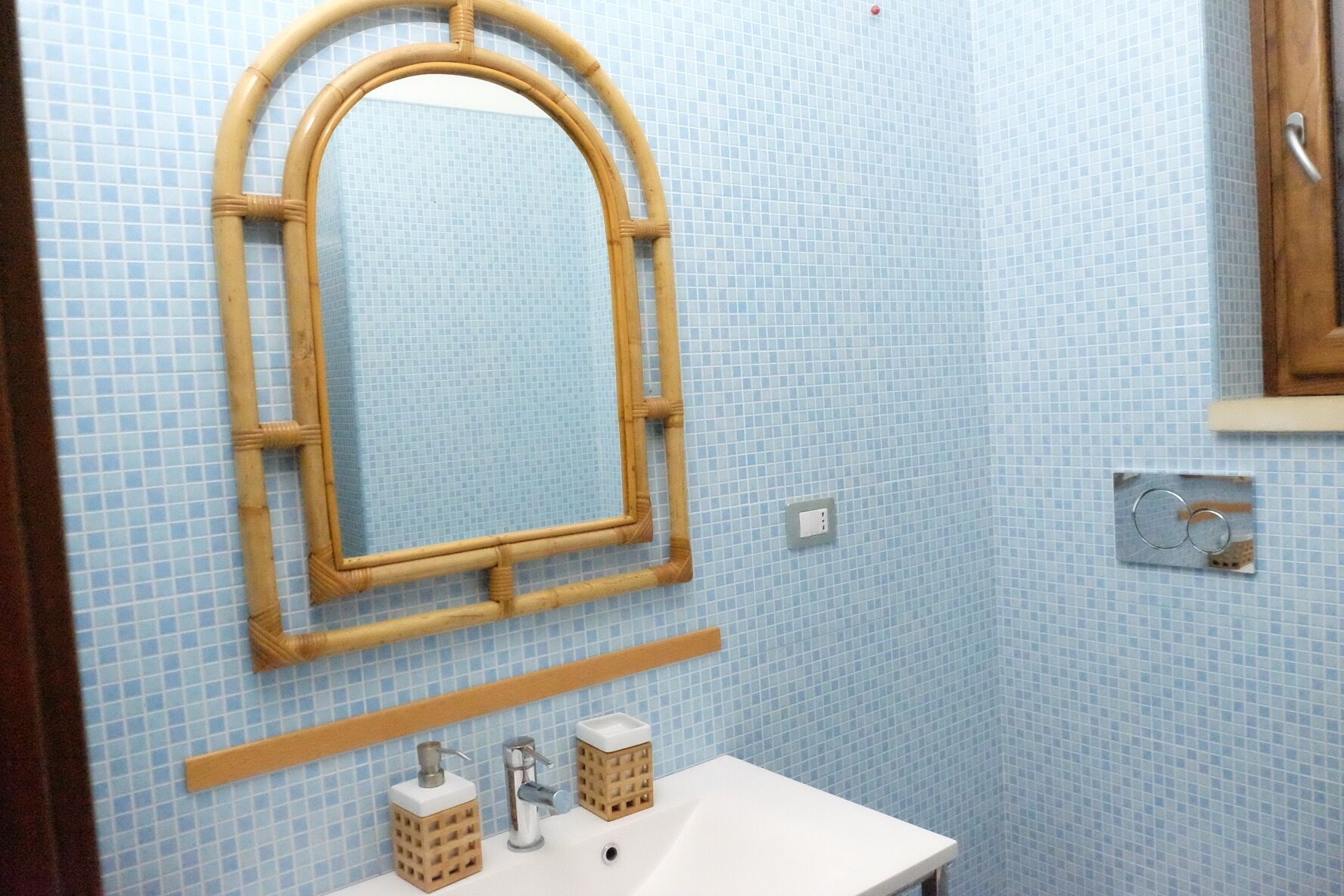 A bathroom with a bamboo-framed mirror, a white sink, and two soap dispensers.