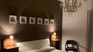 Quarto com uma cama grande, duas mesas de cabeceira com luminárias, um candelabro e quadros nas paredes.