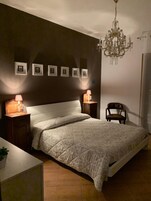 Un dormitorio con una cama grande, dos mesitas de noche con lámparas, un candelabro y cuadros enmarcados en la pared.