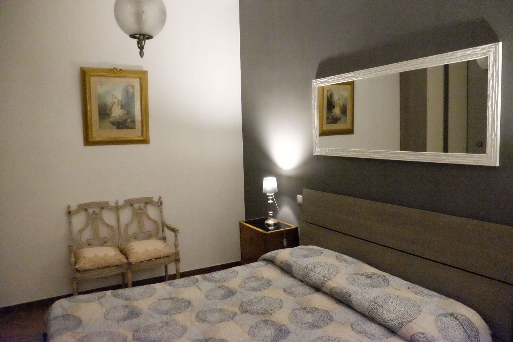 Une chambre à coucher comprenant un lit, une chaise, une table de chevet avec une lampe, et deux tableaux encadrés accrochés au mur.