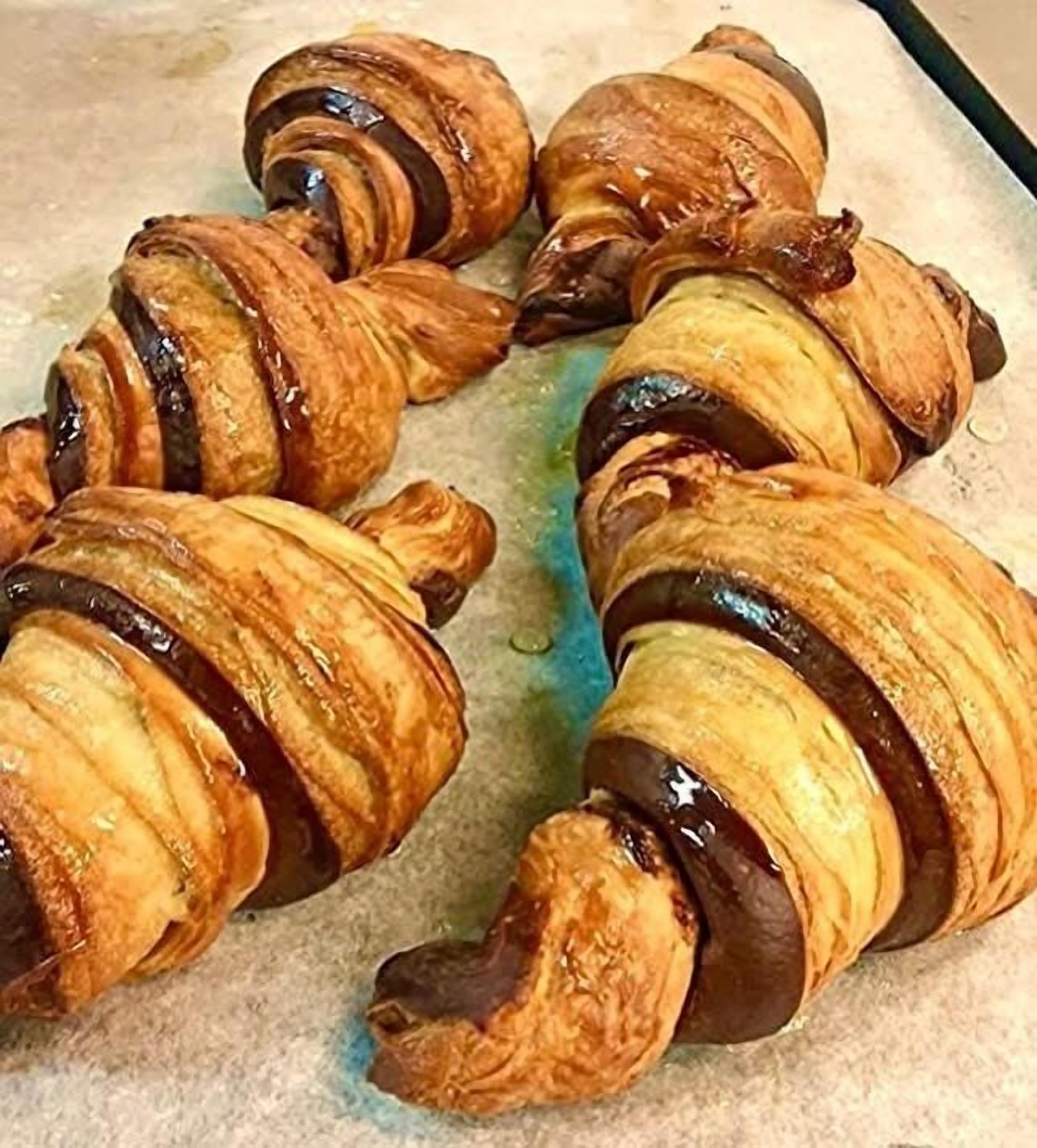 Quatro croissants com cobertura de chocolate em uma assadeira.