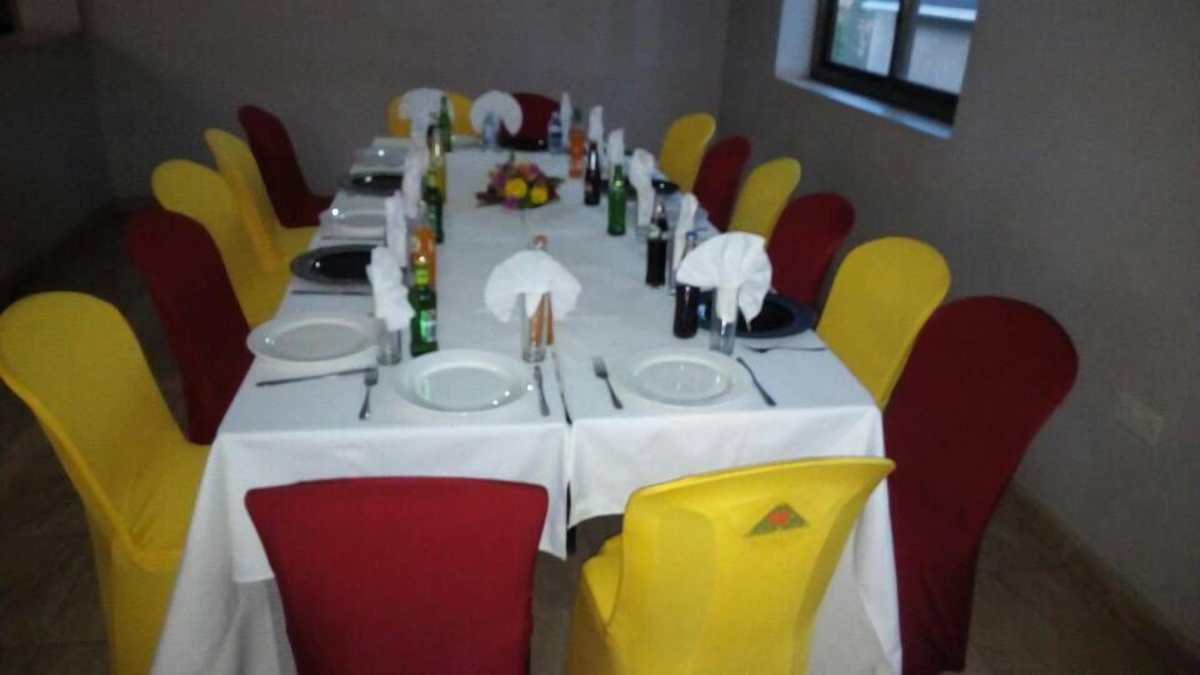 A dining area with a long table set for a meal, surrounded by yellow and red chairs.
