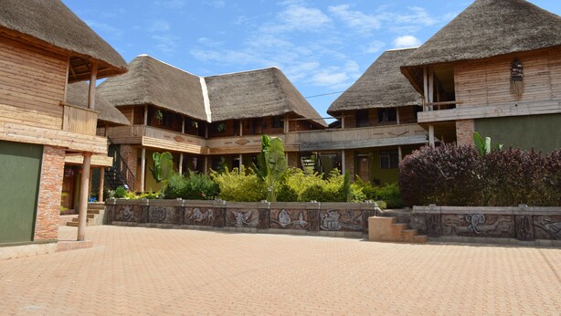 A courtyard with thatched-roof buildings, a paved walkway, and decorative stonework. - Unik Hotel Limited (Kampala)