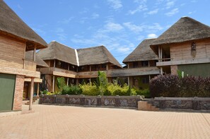A courtyard with thatched-roof buildings, a paved walkway, and decorative stonework. - Unik Hotel Limited (Kampala)