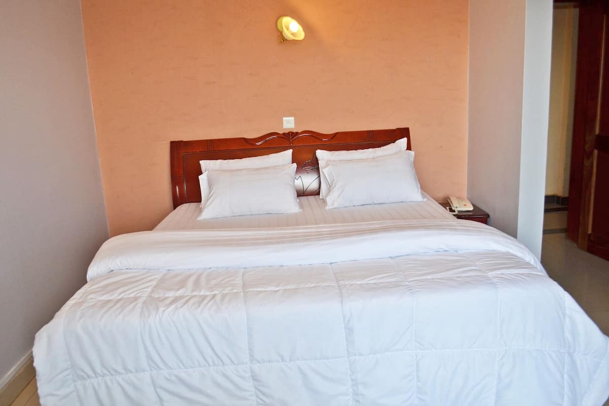 A neatly made bed with white bedding and a wooden headboard in a hotel room.
