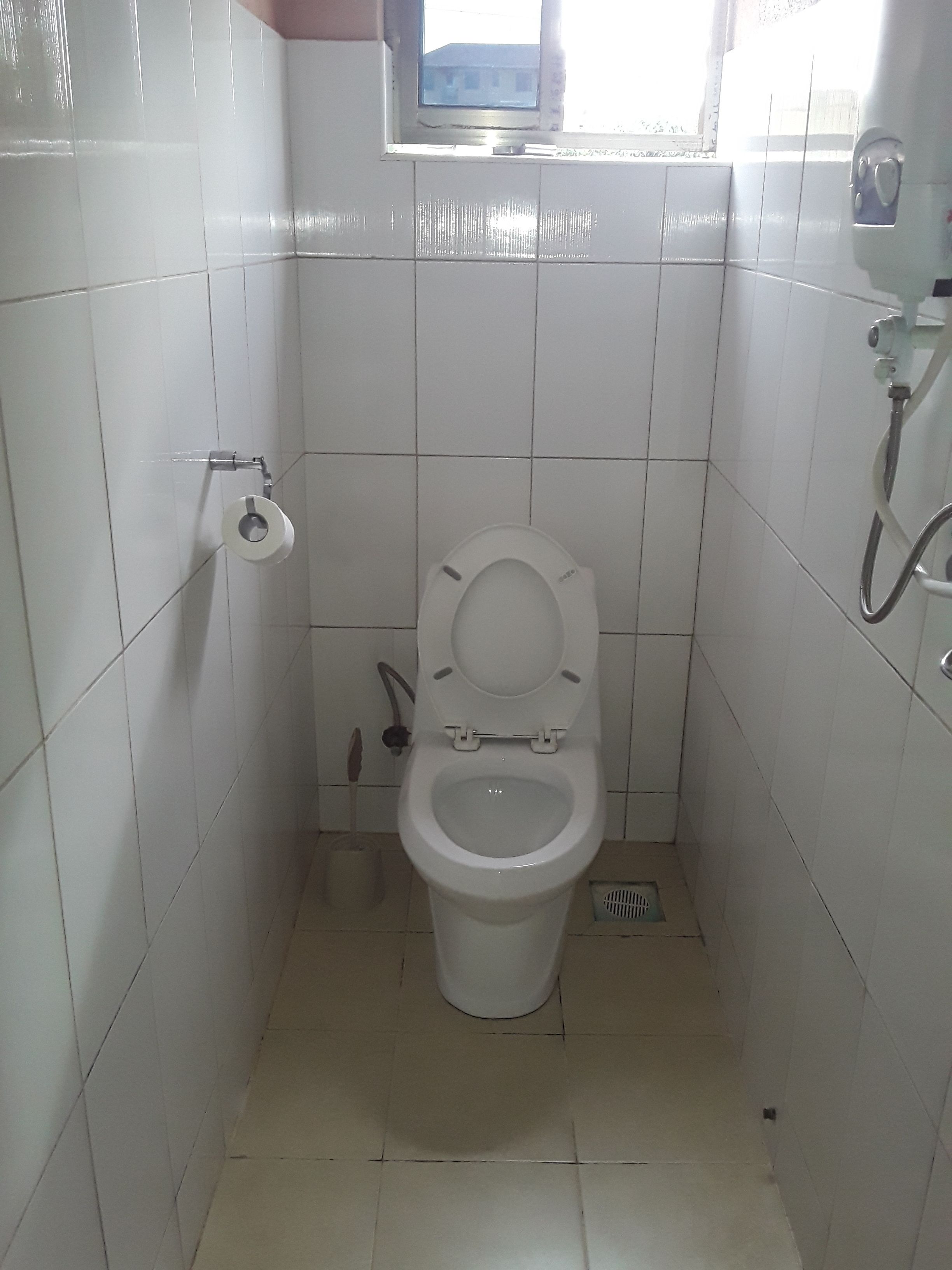 A small, white-tiled bathroom with a toilet, a bidet, and a window above the toilet.