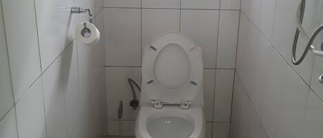 A small, white-tiled bathroom with a toilet, a bidet, and a window above the toilet.