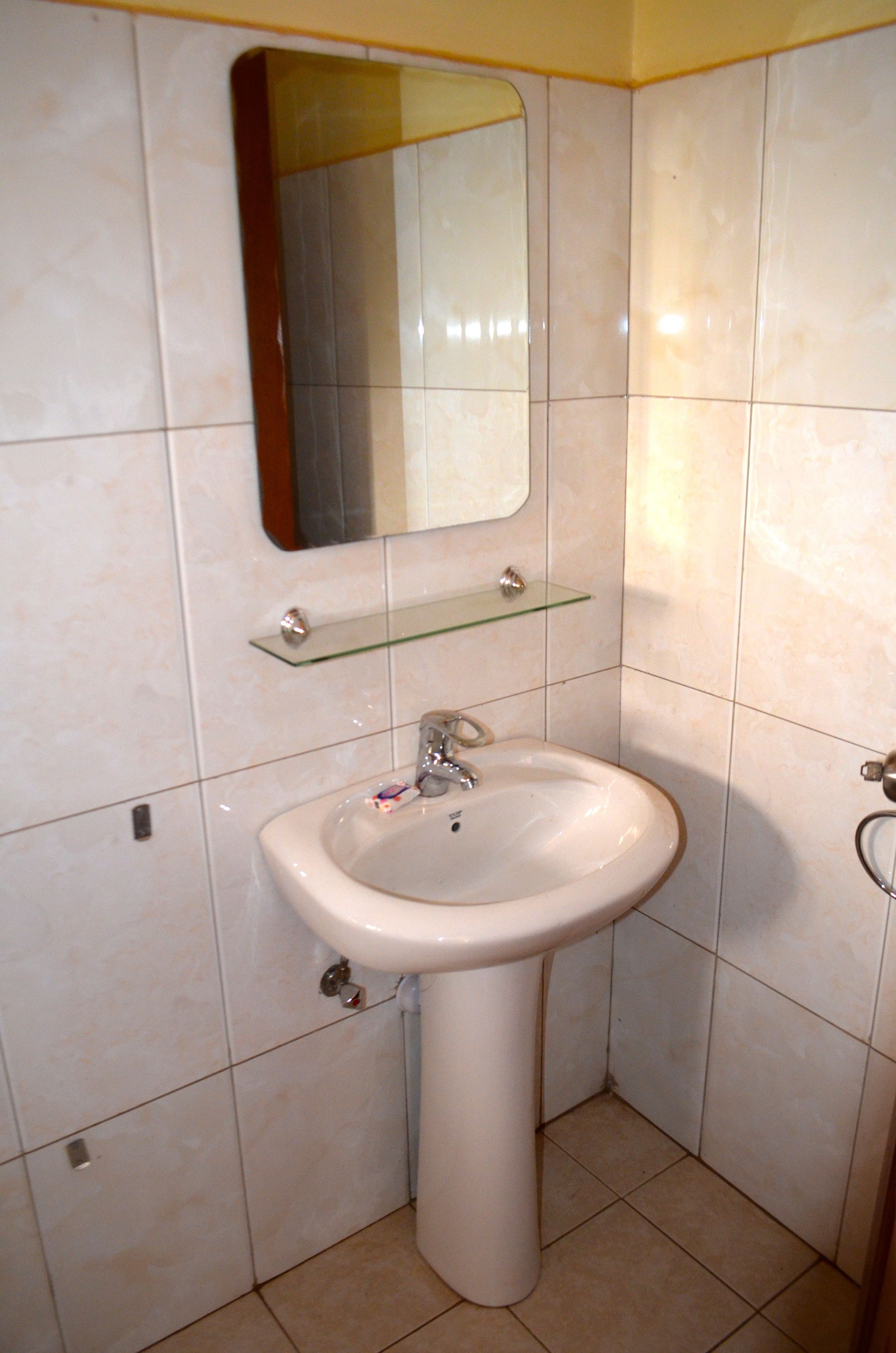 Une salle de bain avec un lavabo sur pied blanc, une étagère en verre au-dessus du lavabo et un miroir au mur.