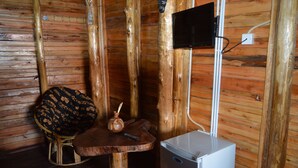 A rustic wooden room with a small table, a stool, a decorative vase, and a white appliance. - Unik Hotel Limited (Kampala)