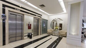 A modern hotel lobby with a black and white striped floor, two elevators, a reception desk, and a seating area with a vase of flowers. - Di Giulio Hotel (São José dos Campos)